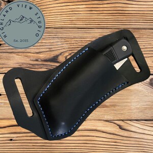 May include: Black leather knife sheath with blue stitching. The sheath has a belt loop and a pocket for a knife.