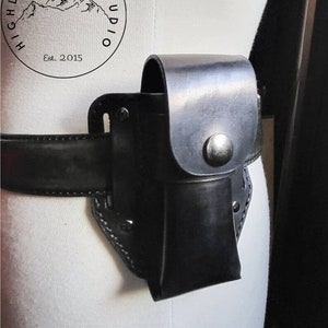 May include: Black leather belt with a black leather holster attached. The holster has a snap closure and is designed to hold a small object. The belt is worn on a white mannequin.