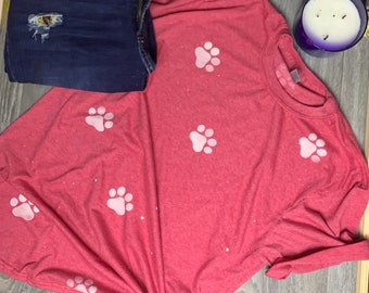 May include: A red t-shirt with white paw prints. The shirt is made of a soft, comfortable material and has a relaxed fit.