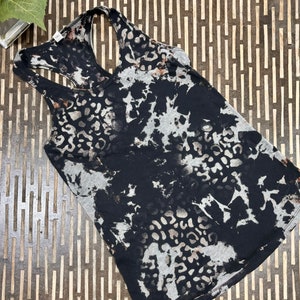 May include: A black and gray tank top with a racerback design. The top features a leopard print pattern with a tie-dye effect. The tank top is made of a soft, lightweight material.