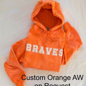 May include: Orange hoodie with the word "BRAVES" in white lettering. Custom orange tie dye available on request.