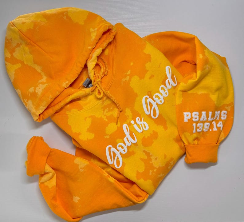 May include: A yellow tie-dye hoodie with the text "God is good" in white on the front and "PSALMS 139:14" in white on the sleeve.