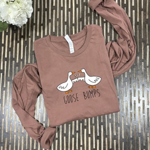 May include: A long-sleeved mauve t-shirt with a graphic of two geese bumping fists and the text "Goose Bumps".