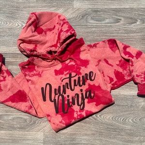 May include: Red tie-dye hoodie with the text "Nurture Ninja" in black lettering.