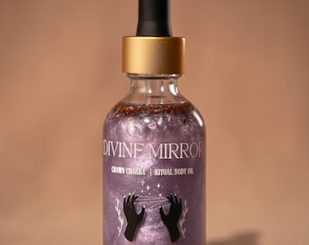May include: A glass bottle with a gold lid and a dropper top. The bottle is filled with a purple liquid and has a label that reads "Divine Mirror Crown Chakra Ritual Body Oil" and "Sacred Sisters Apothecary".