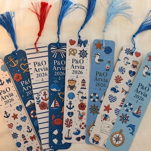 May include: Eight rectangular bookmarks featuring nautical themes, including anchors, ships, and sea life. Each bookmark displays the text P&O Arvia 2026 and is topped with a colourful tassel in shades of blue or red, arranged in a row on a surface.