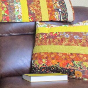 May include: A brown leather couch with two yellow and brown striped pillows and a yellow book on top of the couch.