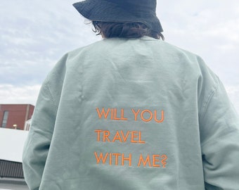 Könnte beinhalten: Ein hellgrüner Pullover mit dem Text "WILL YOU TRAVEL WITH ME?" in orange auf der Rückseite gestickt.