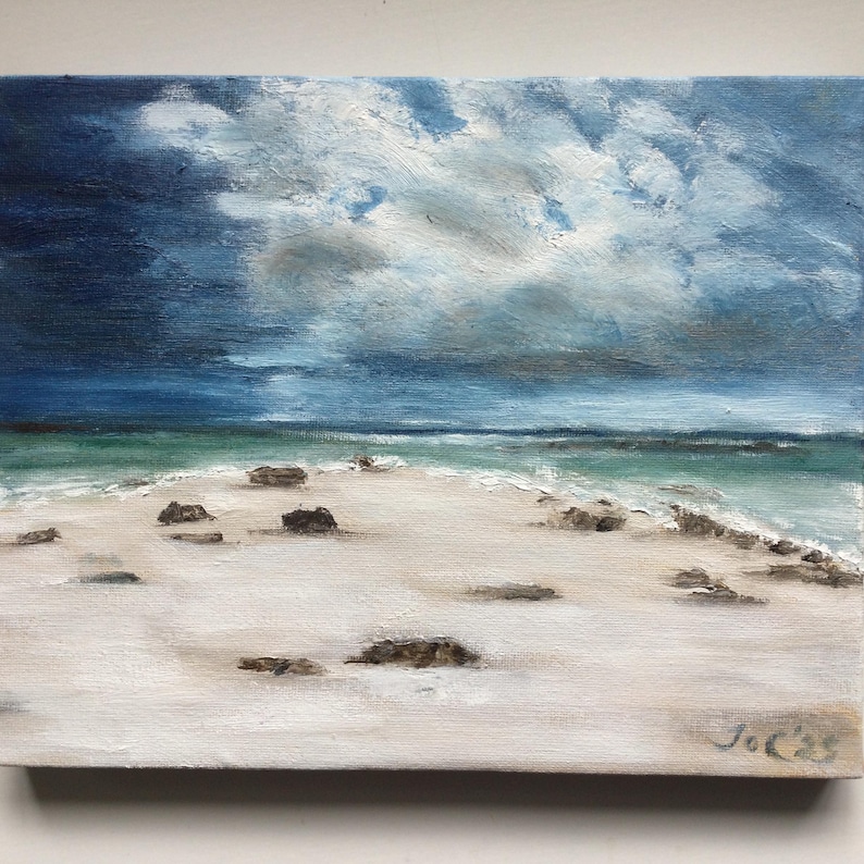May include: An oil painting of a beach scene with a dramatic sky. The sky transitions from dark blue to lighter shades, with fluffy white clouds. The beach has white sand, small rocks, and turquoise water.