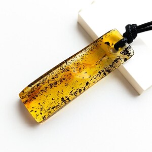 May include: A rectangular amber pendant with black flecks, suspended from a black cord.