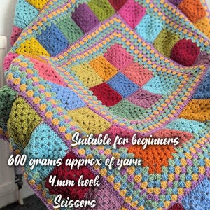 May include: A colorful, handmade crochet blanket with a patchwork design. The blanket features squares in various colors, including yellow, blue, green, pink, and purple. The text on the blanket says "Suitable for beginners", "600 grams approx of yarn", "4mm hook", "Scissors", and "Sewing needle".