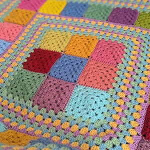 May include: A handmade, colorful crochet blanket featuring a patchwork design. The blanket showcases squares in various shades, including pink, yellow, blue, green, and purple. The squares are bordered by a light blue and orange trim, creating a vibrant and cozy textile.