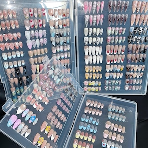 Könnte beinhalten: Nahaufnahme von mehreren durchsichtigen Plastikbehältern, die mit Reihen von bunten Nagelkunstdesigns gefüllt sind. Die Behälter sind in einem Raster angeordnet und auf einer weißen Oberfläche ausgestellt.