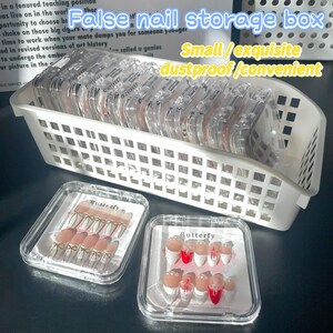 May include: A white plastic storage box filled with clear plastic containers labeled "Butterfly". The containers hold sets of false nails with white and red tips and gold accents. The text "False nail storage box" is written in black on a white background above the box. The text "Small/exquisite dustproof/convenient" is written in black on a white background below the box.