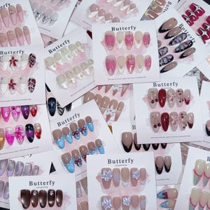 May include: Assortment of fake nail designs with various colors, patterns, and shapes. The designs include cherries, bows, flowers, and butterflies. The designs are labeled "Butterfy nail painting".