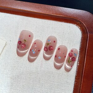Puede incluir: Conjunto de seis u&ntilde;as postizas ovaladas con base rosa claro y dise&ntilde;os de cerezas. Cada u&ntilde;a tiene un dise&ntilde;o de cereza diferente con cerezas rojas, tallos verdes y purpurina azul.