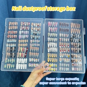 May include: A clear plastic storage box with two rows of compartments for storing nail art supplies. The box is filled with colorful nail tips and rhinestones. The text "Nail dustproof storage box" is printed on the top of the box. The text "Super large capacity super convenient to organize" is printed below the box.