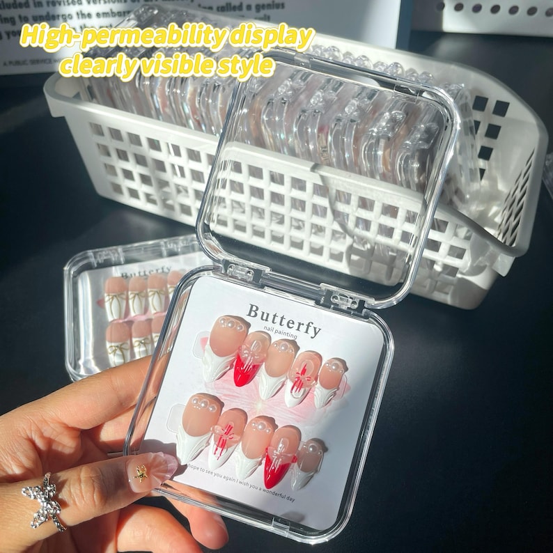 May include: A clear plastic box with a white lid containing a set of false nails. The nails are white with red tips and a white butterfly design. The box has the text "Butterfly nail painting" on the lid.