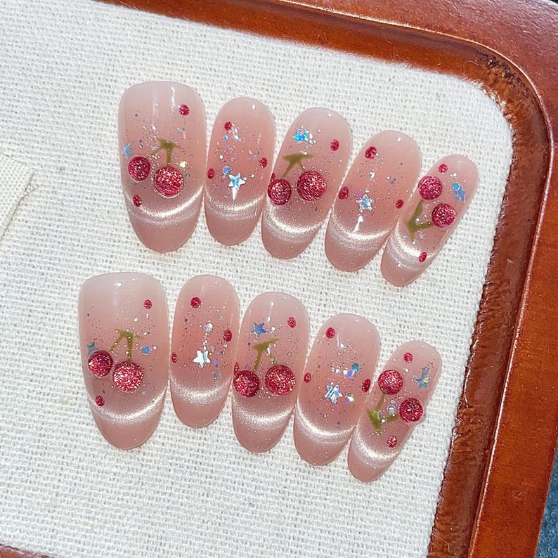 Puede incluir: Conjunto de diez u&ntilde;as postizas de color rosa y blanco con dise&ntilde;os de cerezas y estrellas.