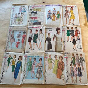 May include: A collection of vintage Simplicity sewing patterns. The patterns feature illustrations of women in various dresses and outfits. The covers are in various colors, including blue, green, and white. The price is printed on the covers.