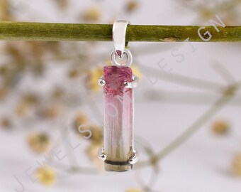 May include: A silver pendant featuring a natural tourmaline crystal. The crystal is a vertical rectangle with a gradient of pink, white, and green hues. The pendant is suspended from a silver bail.