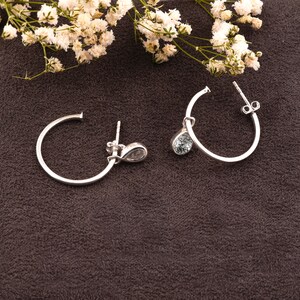 May include: A pair of silver hoop earrings with a teardrop-shaped crystal dangling from each hoop.