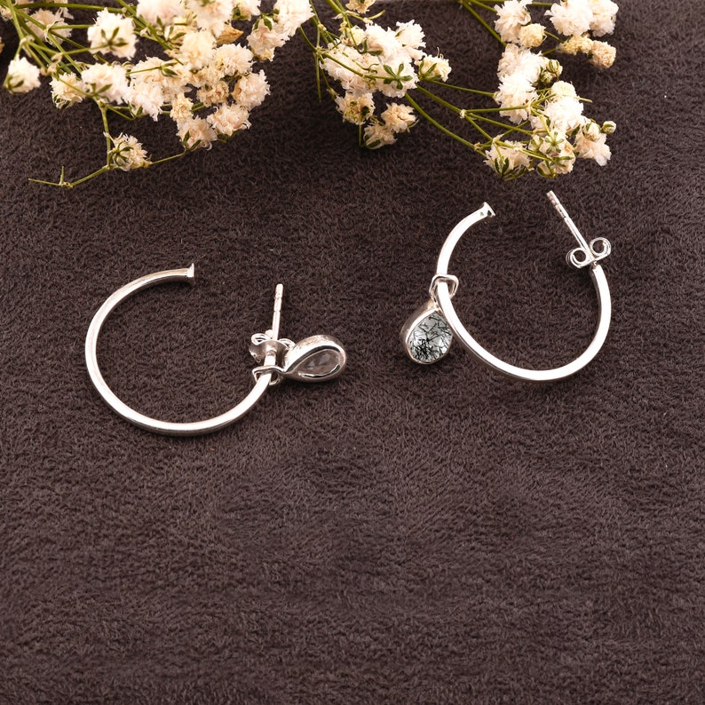 May include: A pair of silver hoop earrings with a teardrop-shaped crystal dangling from each hoop.