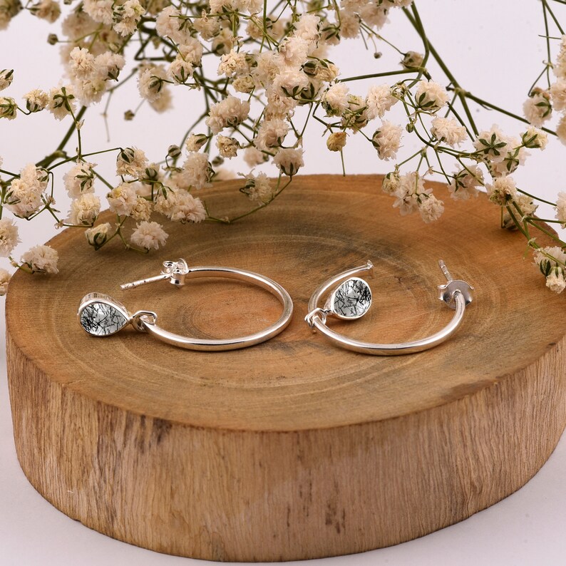 May include: A pair of silver hoop earrings with a teardrop-shaped stone pendant. The stones are clear with a gray and white marbled pattern.