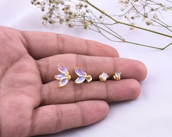 Könnte beinhalten: Vier goldfarbene Ohrstecker mit irisierenden, mondsteinartigen Cabochons. Zwei Ohrringe haben eine dreiteilige, blattartige Anordnung, während die anderen beiden kleinere Ohrstecker mit nur einem einzelnen Stein sind.