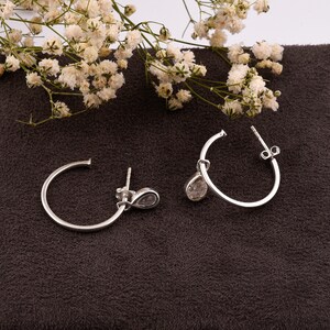 May include: A pair of silver hoop earrings with a teardrop-shaped clear crystal dangling from each hoop.