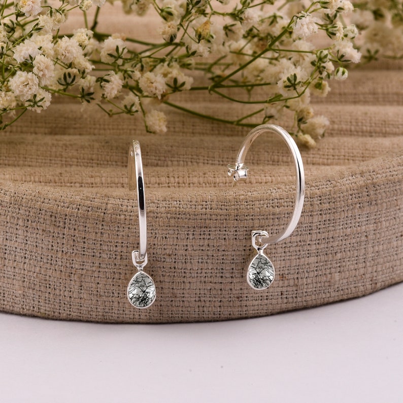 May include: A pair of silver hoop earrings with a dangling teardrop-shaped stone. The stone is clear with black and gray markings.