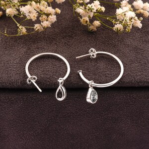 May include: A pair of silver hoop earrings with teardrop-shaped charms. The charms are clear with black flecks.