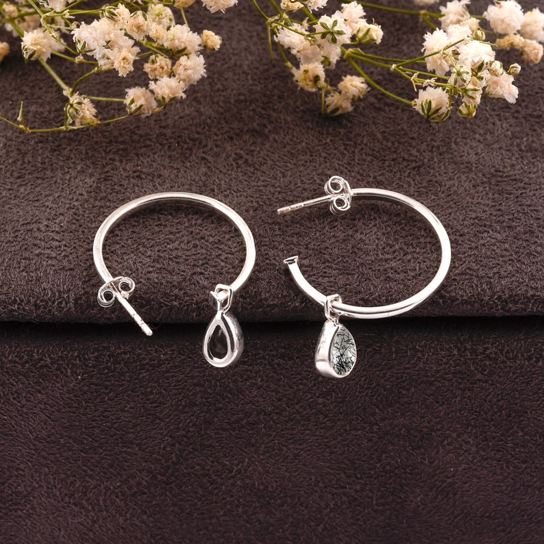 May include: A pair of silver hoop earrings with teardrop-shaped charms. The charms are clear with black flecks.