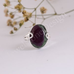 Puede incluir: Anillo de plata con una piedra preciosa ovalada en tonos burdeos y verdes. El anillo tiene un diseño de cuerda trenzada en los lados de la piedra y una banda de plata lisa. Una joya elegante.