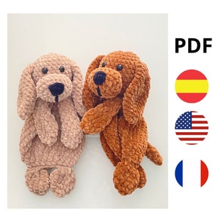 Puede incluir: Dos juguetes de peluche de perro tejidos a crochet, uno marrón y otro marrón claro. Ambos perros tienen ojos y narices negros.