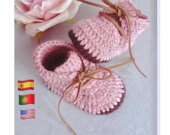 May include: A pair of pink crocheted baby booties with brown leather laces. The booties have a textured stitch pattern and a brown trim around the edges.