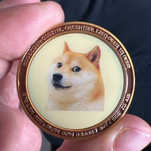 Puede incluir: Una moneda de cobre con una imagen de un perro Shiba Inu y el texto "DOGE COIN DIGITAL DECENTRALIZED PEER TO PEER 1PV 0:2 999 FINE COPPER M3B MONETARY METAL".