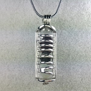 May include: A silver chain necklace with a silver cage pendant containing three round stones. The stones are a dark purple, a dark gray, and a light green.