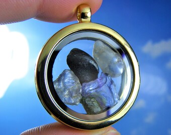 May include: Gold locket pendant with a clear glass window, showcasing a collection of small, colorful gemstones. The gemstones are a mix of blue, purple, and clear.