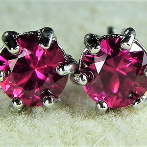 Puede incluir: Un par de pendientes de botón de plata con piedras redondas de color rosa brillante.