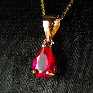 May include: A gold pendant necklace with a teardrop-shaped ruby gemstone.