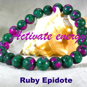 May include: A beaded bracelet made of round, polished ruby and epidote stones featuring a mottled green and vibrant magenta color pattern. The text "Activate energy" is written in purple script, and "Ruby Epidote" is printed in purple below.