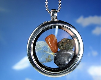 May include: A silver locket necklace with a clear glass window, showcasing four small stones: a clear quartz, a red carnelian, a dark grey stone, and a green stone.