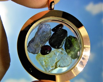 May include: A gold locket pendant with a clear glass insert containing a variety of small, colorful gemstones. The gemstones include blue, green, and red.