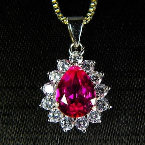 May include: A silver pendant necklace with a large pink gemstone surrounded by smaller clear gemstones.