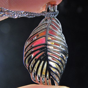 May include: A silver leaf-shaped cage pendant necklace with a clear glass orb inside. The cage is detailed with intricate lines and the orb has a pink and yellow iridescent shimmer.