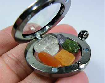 May include: A silver locket with a clear glass lid, open to reveal five small stones: a clear quartz, a light orange carnelian, a yellow citrine, a green aventurine, and a purple amethyst.