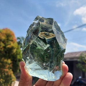 Puede incluir: Una gran roca de vidrio verde claro con una forma irregular y rugosa. La roca es transl&uacute;cida y tiene un aspecto ligeramente nublado. Se est&aacute; sosteniendo en la mano de una persona.