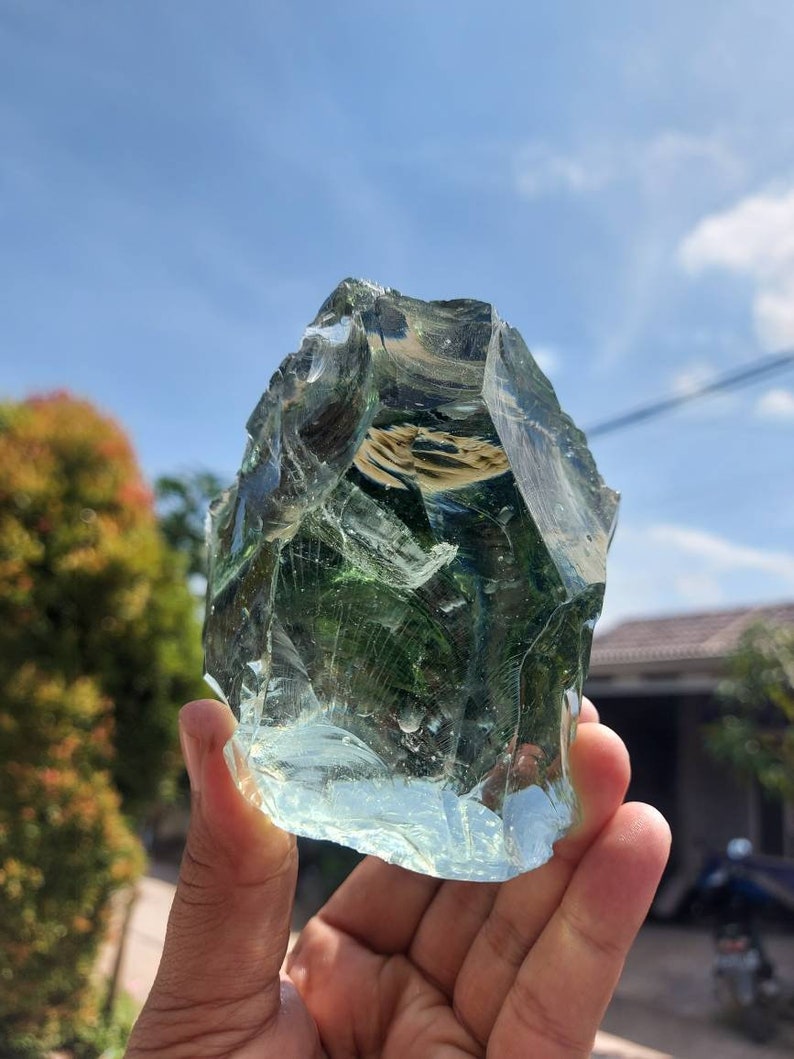 Puede incluir: Una gran roca de vidrio verde claro con una forma irregular y rugosa. La roca es transl&uacute;cida y tiene un aspecto ligeramente nublado. Se est&aacute; sosteniendo en la mano de una persona.