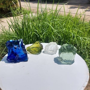Puede incluir: Cuatro piedras de vidrio de diferentes colores: azul, verde, amarillo y transparente. Las piedras est&aacute;n sobre una mesa blanca.